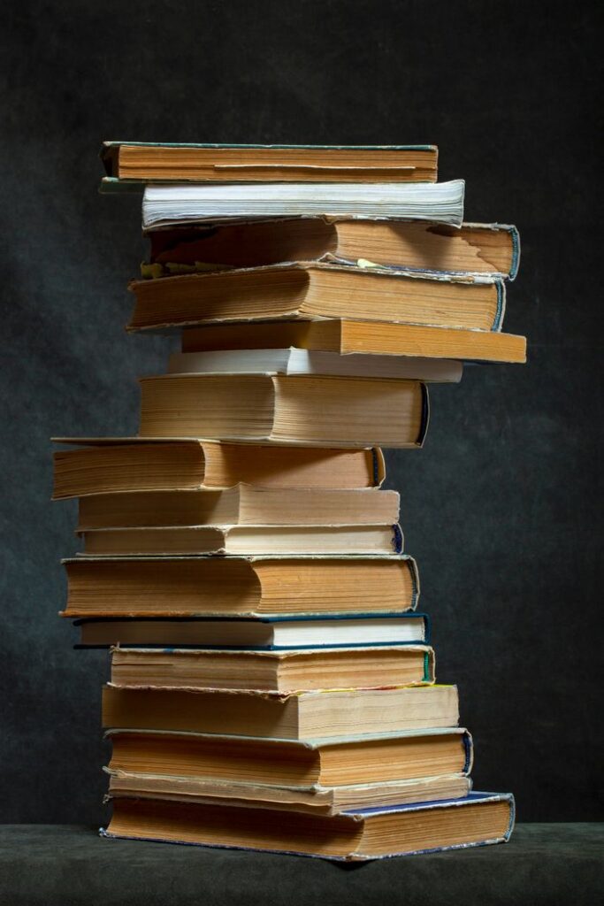 A towering stack of vintage books with weathered pages on a dark, textured background.